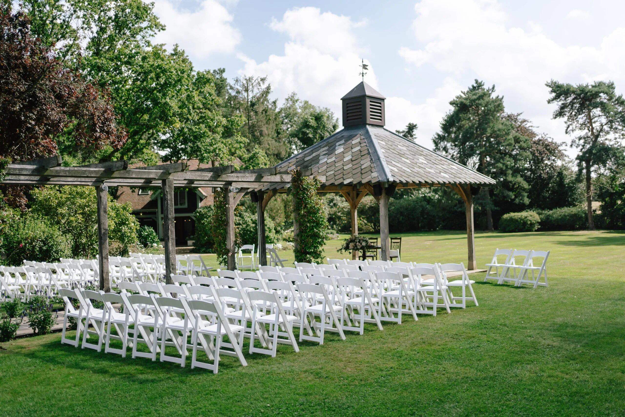 Outdoor wedding ceremony setup with white chairs and garden gazebo